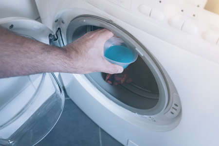 male hand placing measuring cap with laundry detergent in washerの写真素材