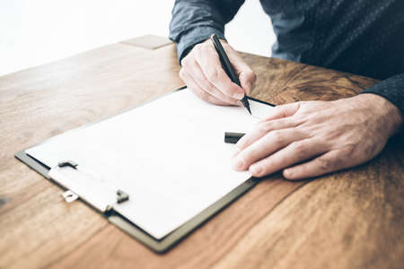 close-up shot of businessman signing contract or document on wooden deskの写真素材