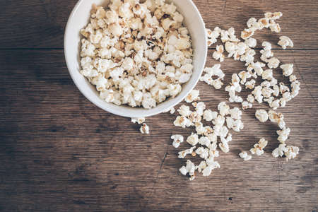 top view of bowl filled with popcorn and spilled popcorn on rustic wooden tableの写真素材