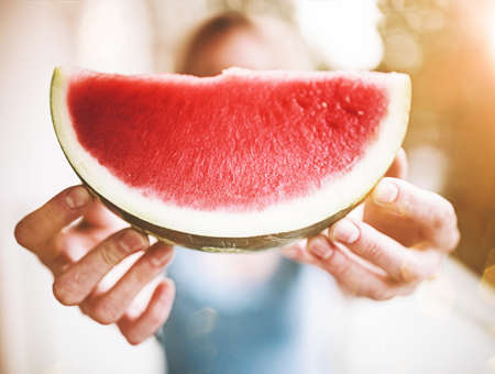front view of blond woman holding a slice of juicy fresh watermelon