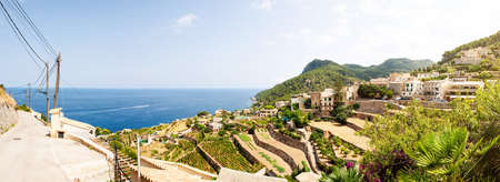 Panoramic shot of typical village and landscape against blue sea and sky on island of Mallorca,...