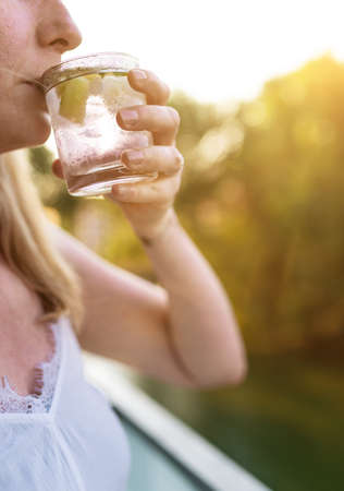 close-up of blond woman outdoors on summer day drinking iced drink