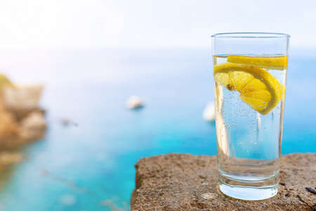 close-up of drinking glass with cold carbonated water or soft drink and lemon slice against blue sea...