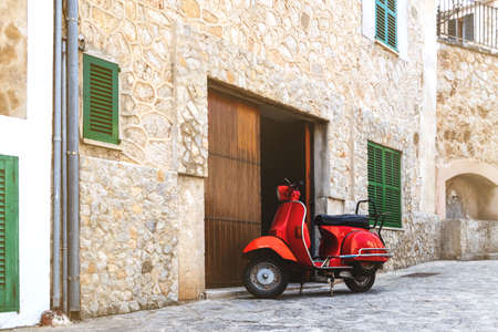 vintage red motor scooter parked on cobbled street in hostoric spanish villageの写真素材