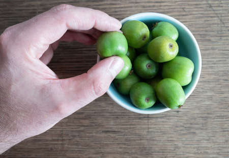 cropped hand picking hardy kiwi fruit or kiwi berry from ceramic bowl on wooden kitchen tableの写真素材
