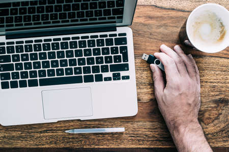 top view of man connecting USB thumb drive to laptop computerの写真素材
