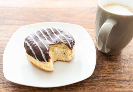 high angle view of chocolate coated jelly doughnut and cup of coffee on wooden tableの写真素材