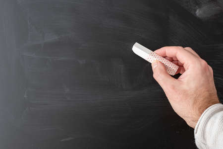 hand holding stick of chalk against dirty blackboard templateの写真素材