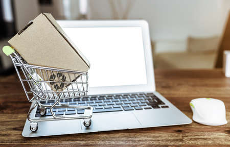 online shopping concept with miniature shopping cart and laptop computer on wooden table