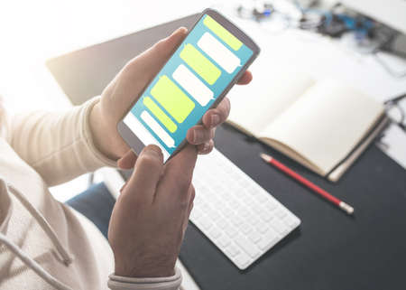 close-up of person using messaging app mock-up on smartphone at office deskの写真素材