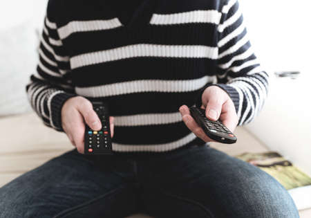 close-up of man sitting on sofa holding remote control in each handの写真素材