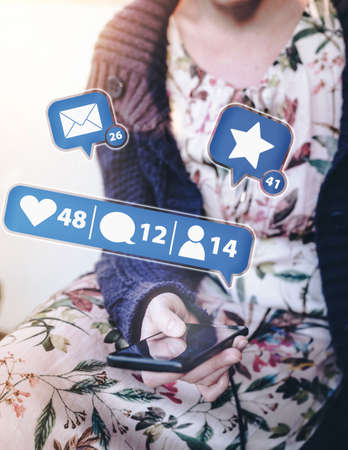 young woman in long dress and cardigan sitting outside on porch using smartphone with social media...