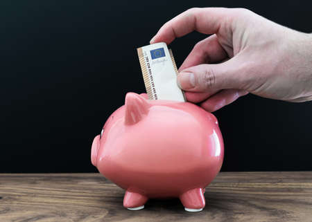 close-up of hand putting money in piggy bankの写真素材