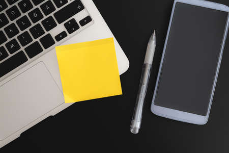 adhesive note on laptop computer next to smart phone and pen on dark background
