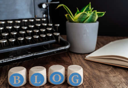 word BLOG on wooden blocks against vintage typewriter, potted plant and note pad on tableの写真素材