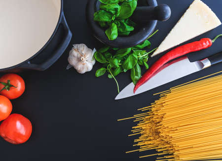 preparing italian pasta with fresh basil in mortar, tomatoes, garlic, pepper and Parmesan cheese on dark kitchen counterの写真素材