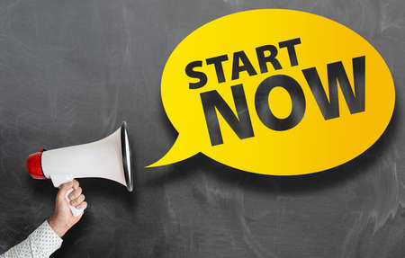 text START NOW in speech bubble and hand holding megaphone against blackboard