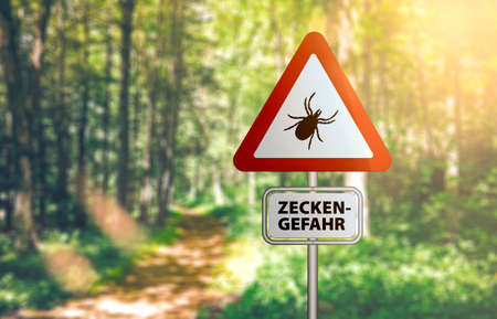 close-up of warning sign with text ZECKEN GEFAHR, German for beware of ticks, against defocused...