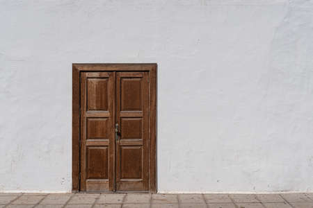 rustic brown wooden entrance door in weathered white wall