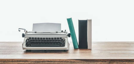 close-up low angle view of vintage typewriter and books on rustic wooden table against white backgroundの写真素材