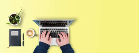 work at home and home office concept, top view of person typing on laptop computer on desk with potted plant, note pad and coffee mugの写真素材