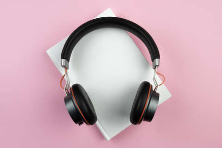 audiobook concept, top view of stereo headphones on hardcover book on pink desktopの写真素材