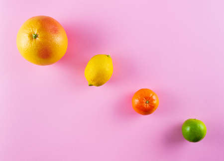 top view of different colorful citrus fruits in a row on pink backgroundの写真素材