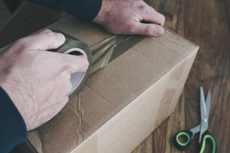 close-up of person sealing up shipping box with parcel tape, pruchase return and return of goods conceptの写真素材