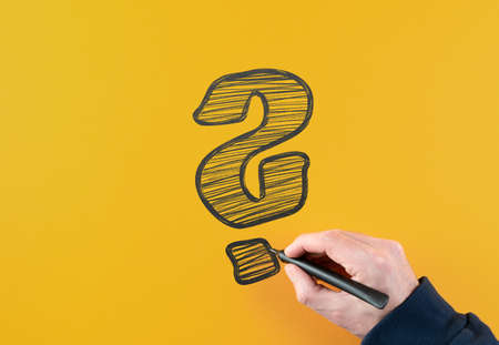 top view of man holding felt tip pen drawing large question mark on orange background