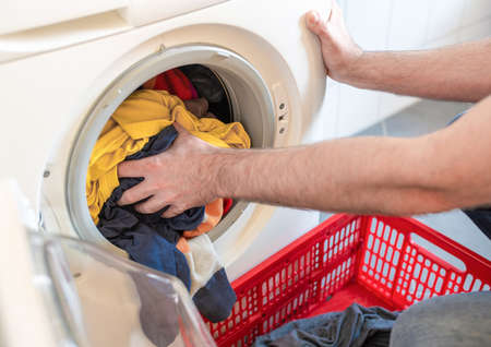 close-up of man loading colored clothes in washing machineの写真素材