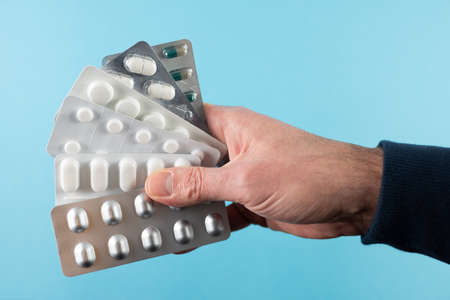 close-up of hand holding medication blister packs of tablets and capsules against blue backgroundの写真素材