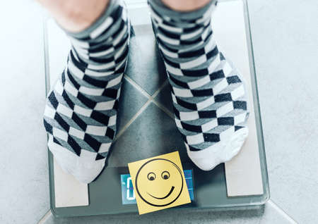 close-up of person in socks on bathroom scale with smiley face, ideal body wight concept