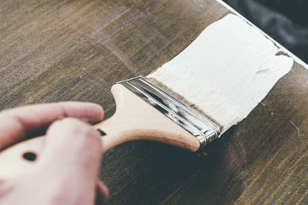 close-up of hand using brush to lacquer wooden furniture with white paintの写真素材