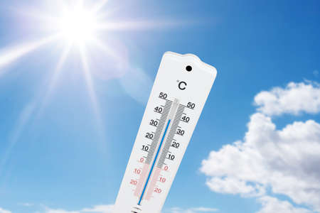 outdoor thermometer indicating high temperatures against blue summer sky and sunの写真素材