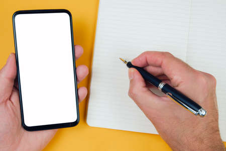 top view of person taking notes on paper while using smartphone, template with copy space