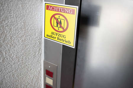 yellow service sign with German text for ELEVATOR OUT OF SERVICE attached to elevator door, digital compositeの写真素材