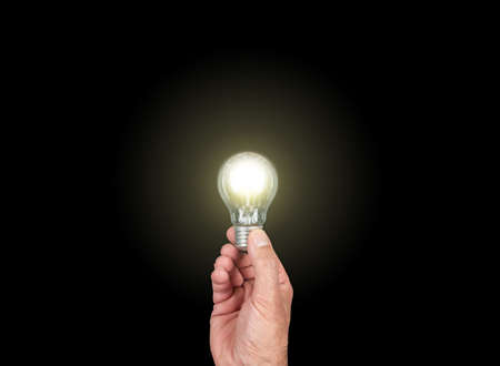 hand holding glowing light bulb against black background, having an idea concept