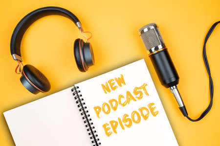 NEW PODCAST EPISODE text on notepad next to headphones and recording microphone, podcasting concept on orange backgroundの写真素材