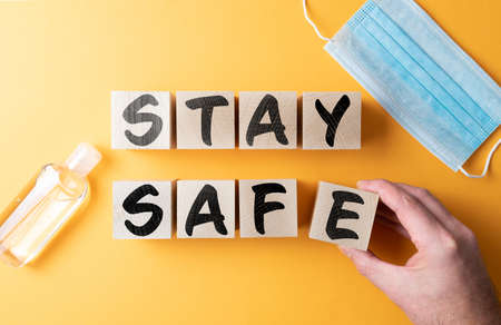 words STAY SAFE on wooden blocks on orange background with protective face mask and hand sanitizer