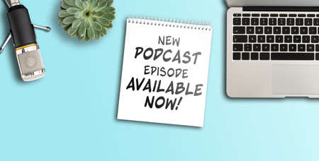 top view of text NEW PODCAST EPISODE AVAILABLE NOW on notepad on desk with microphone and laptop...