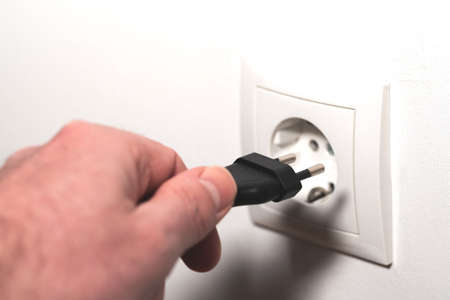 close-up of hand inserting power cord plug into wall outlet or pulling plug from socketの写真素材