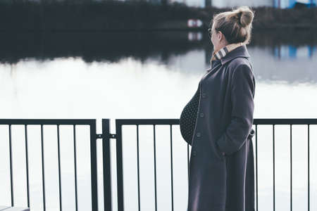 side view of heavily pregnant blonde woman looking at riverの写真素材