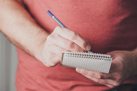 close-up of man taking notes on small spiral notepad using a pencilの写真素材