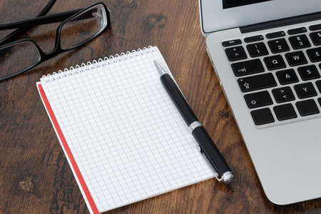 Pen and blank spiral notepad with quad-rules paper next to laptop computer on wooden tableの写真素材