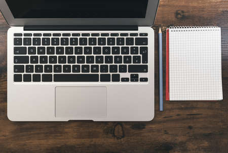 top view of laptop computer and blank note pad with pencil on wooden deskの写真素材