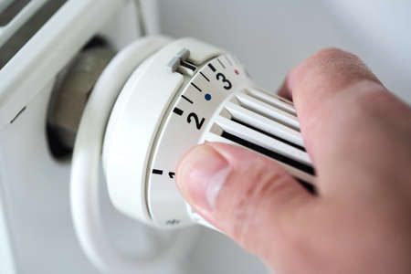 person adjusting thermostat on radiator to lower temperature, saving energy and money conceptの写真素材