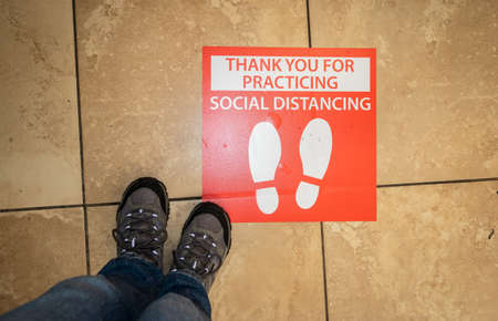 Photo of person's legs and hiking boots near a red thank you for practicing social distancing sign at a supermarket.のeditorial素材