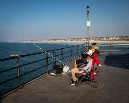 A young masked man sits in a group of fishermen on the Huntington Pier waiting for a bite.のeditorial素材