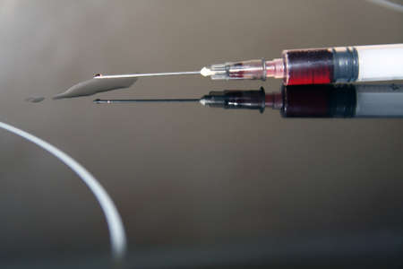 Injection spilling red fluid on a black reflective surfaceの写真素材