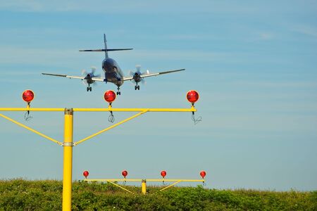 Aircraft landing over runway lights against bright blue skyの写真素材